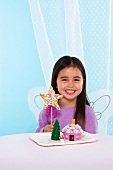 Mädchen mit Engelsflügeln, sternförmigem Cake Pop und Fairy House Cakes auf einem Teller