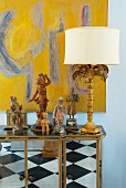 Antiques and table lamp on mirrored, semi-high cabinet in front of modern image on wall