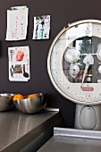 Old industrial scales next to bowl of oranges on stainless steel worksurface and children’s drawings