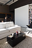 Sunny interior with black-painted travelling trunk as coffee table in front of white sofa