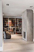 Minimalist interior with open-plan fireplace in concrete wall opposite armchair in front of fitted bookshelves