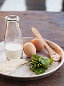 Quiche Zutaten auf einem Tablett (Milch, Eier, Spinat, Ziegenkäse, Parmesan)