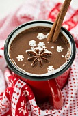 A cup of hot chocolate with star anise, a cinnamon stick and snow flakes