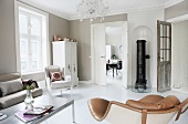 Different armchairs in renovated interior with walls painted pale grey and round iron stove in niche