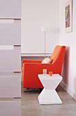 Sitzecke mit skulpturalem Beistelltisch aus Kunststoff und orangefarbenem Polstersessel
