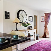 Open-plan interior with console table below wall clock; kitchen counter in foreground