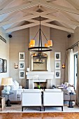 Elegant lounge area with open fireplace below wrought iron candle chandelier hanging from wooden roof structure