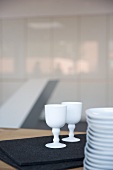 Porcelain goblets on black felt mat next to stacked plates on table