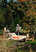 Frau mit Hut und Fellweste, sitzend und lesend an sonniger Lagerstelle im Wald