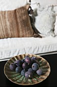 Purple figs on ceramic dish; pale sofa with scatter cushions in background