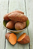 Whole sweet potatoes in a dish, with a halved sweet potato to the front