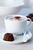 A cup of cappuccino and a praline in the shape of a ring cake