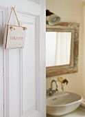 Sign reading 'Toilettes' on open door showing view of washstand and mirror beyond