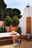 Patio lounge with a straw hat in front of a small tree in a pot in the corner of the terrace of a Mediterranean home with an outdoor shower