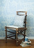 Pillows on a DIY tree branch chair next to stack books on the floor in front of a wall with bright blue wall paper with a floral pattern