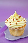 A cupcake with vanilla icing and gold sugar pearls in a paper case