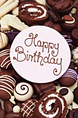 Happy Birthday Schriftzug auf einer Glasurscheibe auf Schokoladenkuchen und Konfekt