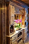 Potted orchid in serving hatch integrated into rustic, wooden fitted cupboard with carved details