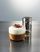 A cappuccino and a cocoa sprinkler on a polished metal surface