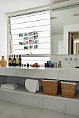 Weisses Marmorbad mit Flaschen auf dem langen Waschtisch und Milchglasfenster mit Fotos neben großem Wandspiegel