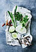 Spring onions, fennel, limes, chilli peppers and prawns on newspaper