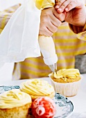 A child's hands using a piping bag full of icing to decorate cupcakes