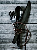 A leather thong wound around a set of cutlery, on a wooden table