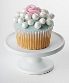 A cupcake decorated with pale blue glaze, sugar pearls and a sugar rose