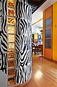 Foyer with zebra patterned curved wall and yellow-painted wall next to open-plan dining room