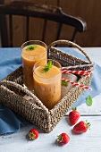 Two fruit smoothies in a woven basket tray, and some strawberries