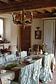 Dining area in rustic kitchen-dining room festively decorated with elegant fabric draped on long dining table and romantic covers on chairs