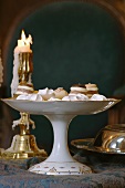 Chocolates and other confectionery on china cake stand in front of lit candle in brass candlestick