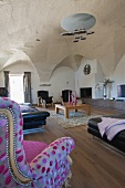 Black leather sofa and reading chair with patterned upholstery in spacious living room with designer lamp hanging from vaulted ceiling