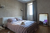 Doppelbett mit gepolstertem Kopfteil an Wand und Spiegel mit Goldrahmen auf Boden neben Fenster