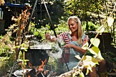 A woman stirring a pot hanging over the campfire