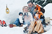 Paar sitzt beim Lagerfeuer im Schnee
