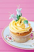 A cupcake decorated with yellow frosting and blue sugar flowers