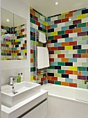 Bathroom with washstand and mirrored cabinet next to bathtub against wall with colourful tiles