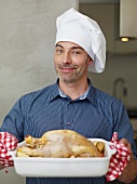 A chef presenting a roast chicken in the roasting dish