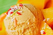 A scoop of mango ice cream with fresh mango pieces and colourful sugar strands