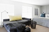 Dunkelgraue Sofakombination und Beistelltische aus Geflecht neben Doppelbett in modernem Schlafzimmer mit geschlossenen Jalousien