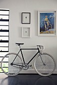 Racing bicycle on dark wooden floor below retro poster and miniature artworks
