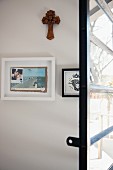 Wooden cross and framed pictures behind French window with horizontal glazing bars and metal frame