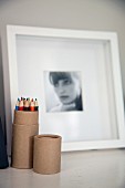 Coloured pencils in cardboard tube and black and white photographic portrait of woman in blurred background