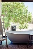 Freistehende Designer Badewanne vor Glasfront und Blick in sonnigen Garten