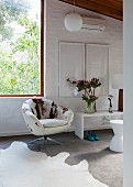 Swivel lounge chair with cow-skin cover next to window; framed pictures above white bench against whitewashed brick wall