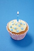 A cupcake topped with pale blue chocolate beans and a candle