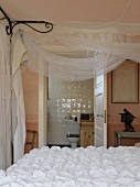 Bed with white bedspread and voile draped from canopy frame; bathroom in background