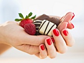 Hand holding chocolates a raspberry and a strawberry