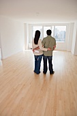 Rear view of couple with blueprints in empty room